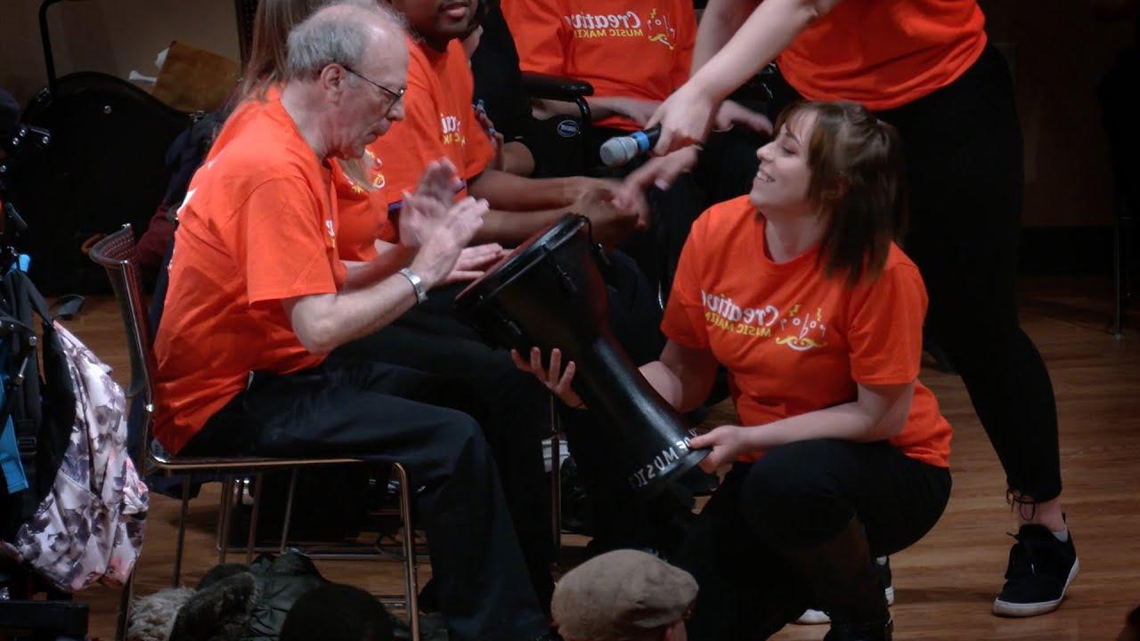 creative music participants interacting with a hand drum; a woman holding the drum while an male elder uses it